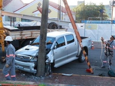 Frente do veículo ficou destruída; funcionários da Energisa trabalham na troca do poste (Foto: Henrique Kawaminami)