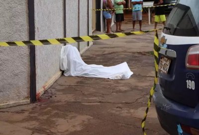 Corpo da vtima escorado no muro de uma casa e coberto com um lenol branco (Foto: Osmar Veiga)